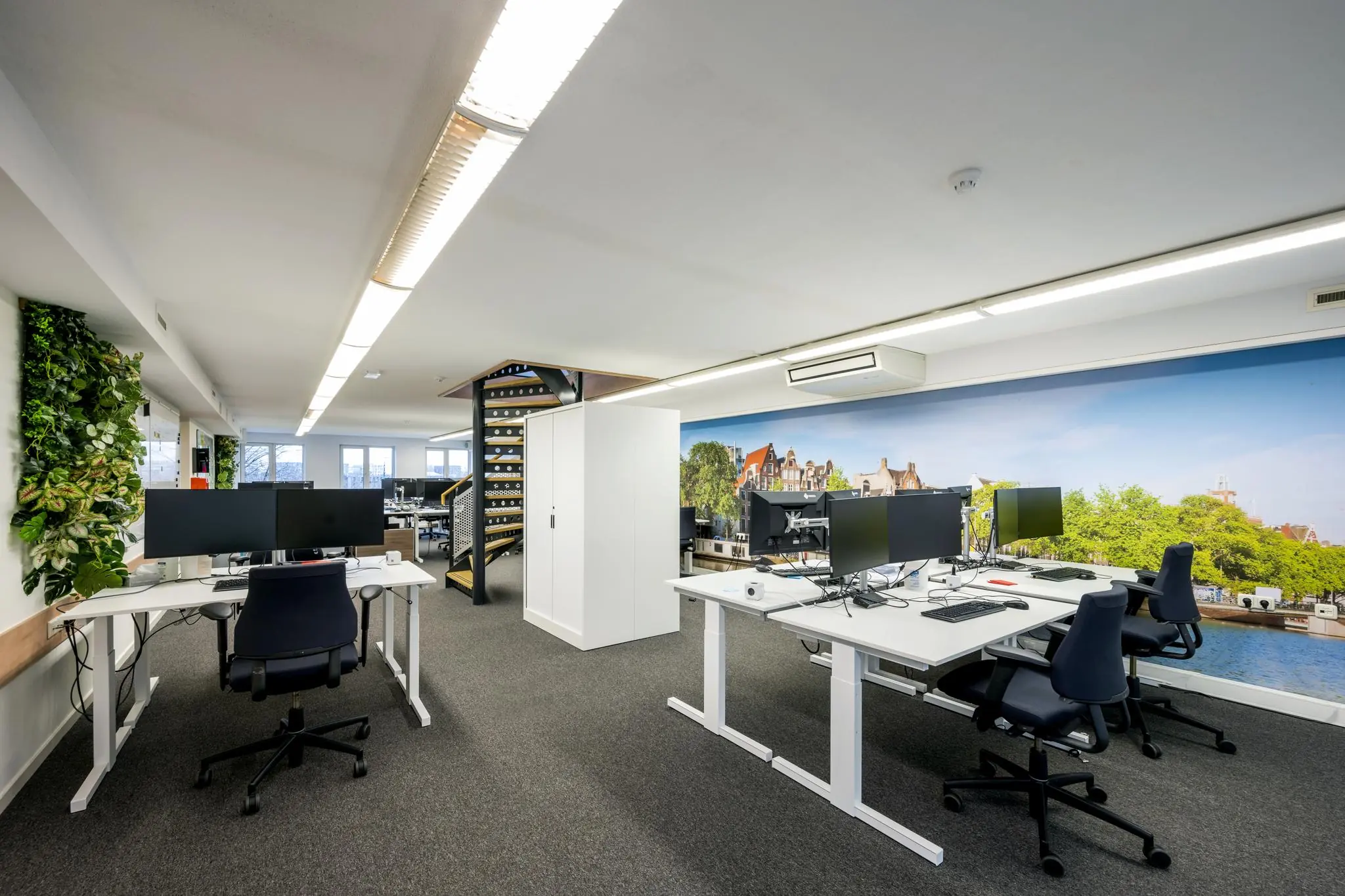 Modern kantoorinterieur aan de Prins Hendrikkade met meerdere werkplekken en een muurfoto van Amsterdamse grachtenpanden.